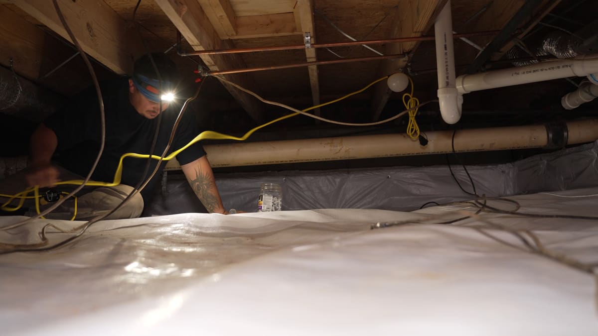 A specialist inspecting a lined crawl space with a headlamp