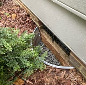 Gravel inside an exterior metal vent well at the base of a house