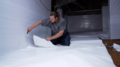 A worker fitting vapor barrier material inside a crawl space.