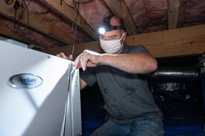 A worker wearing a headlamp installing a crawl space dehumidifier.