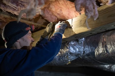 A specialist inspecting wood framing and insulation under a home.