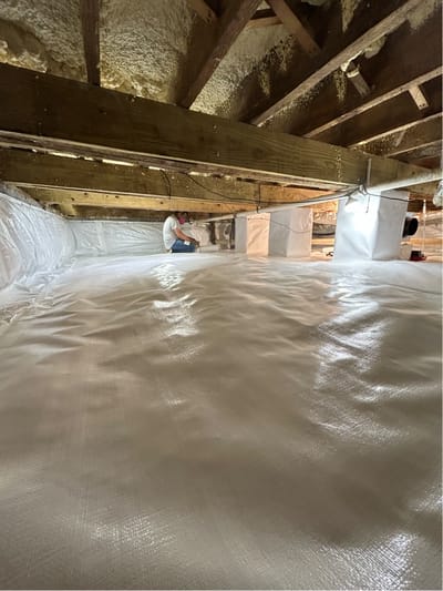 A team member working at the far end of a crawl space lined with white vapor barrier.