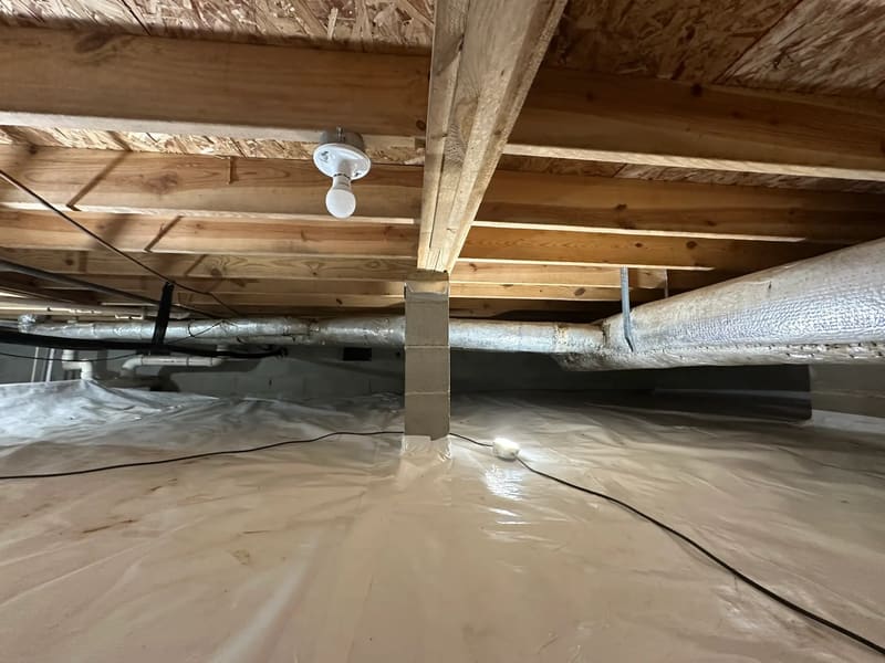 Floor framing, insulation, and a ground liner inside a crawl space