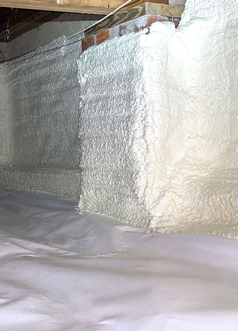 Spray foam on a foundation wall above a white crawl space liner