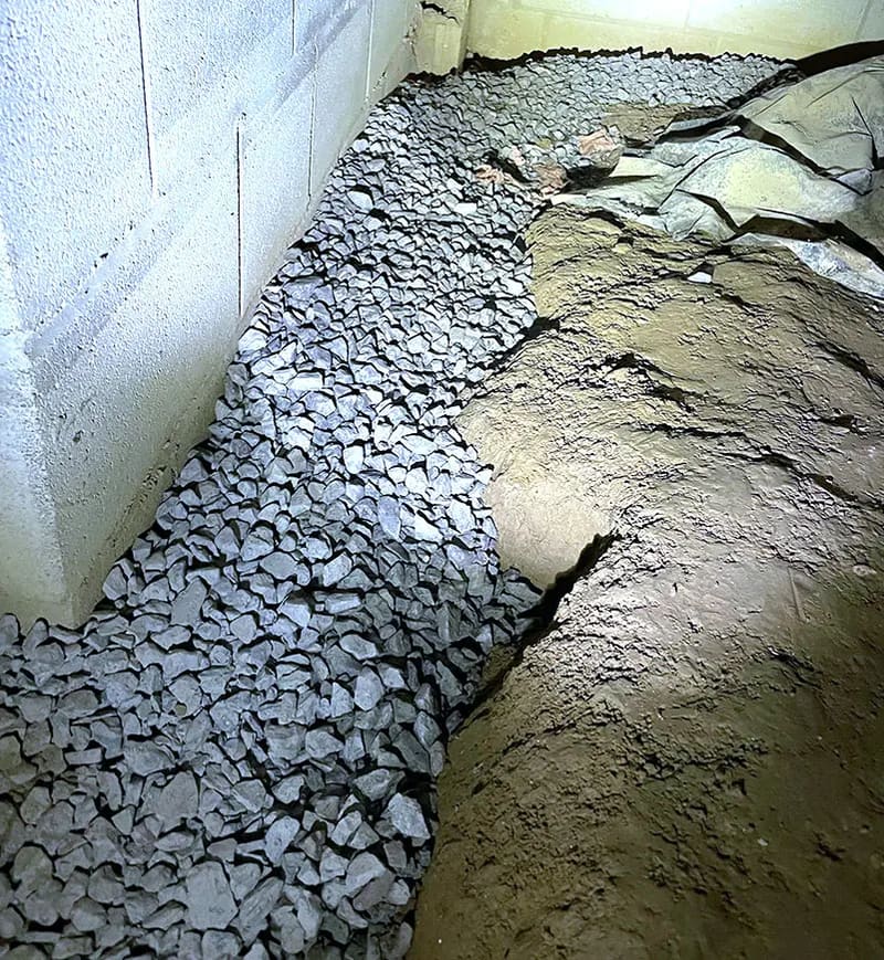 A gravel-filled drainage path beside a crawl space foundation wall