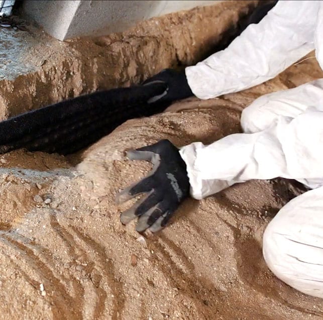 A technician installing drainage material in a trench inside a crawl space