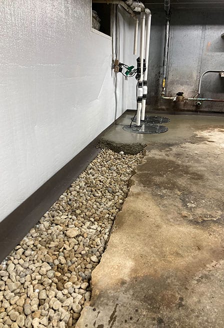 Washed stone filling a drainage trench alongside a basement wall