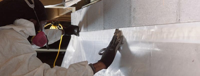 Technician installing a vapor barrier on a crawl space wall