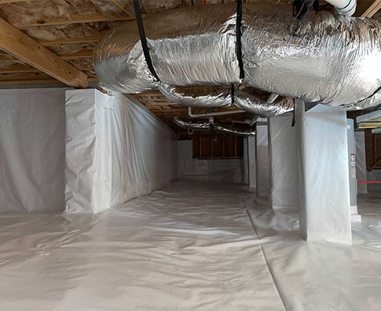 An encapsulated crawl space with white vapor barrier over the floor, walls and piers, and insulated ductwork overhead