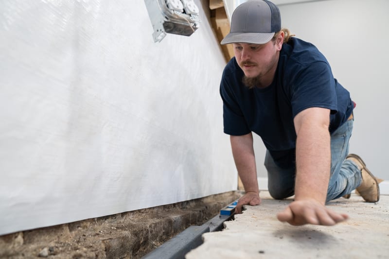A technician fitting drainage along a foundation wall