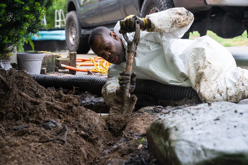 A technician fitting drainage material into a trench inside a crawl space