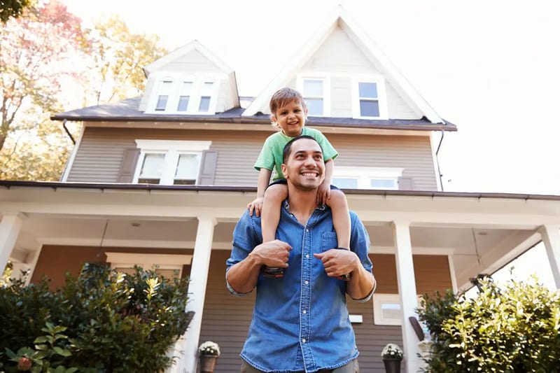 A man carrying a child on his shoulders outside a home