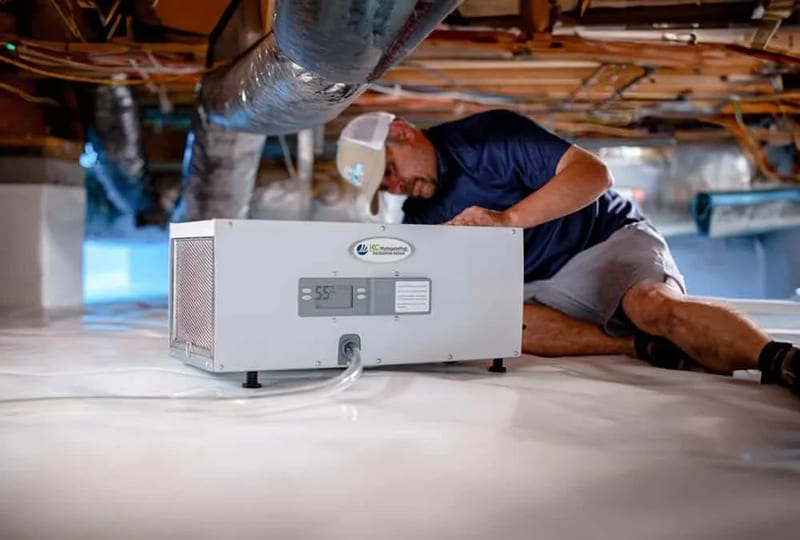A technician servicing a crawl space dehumidifier